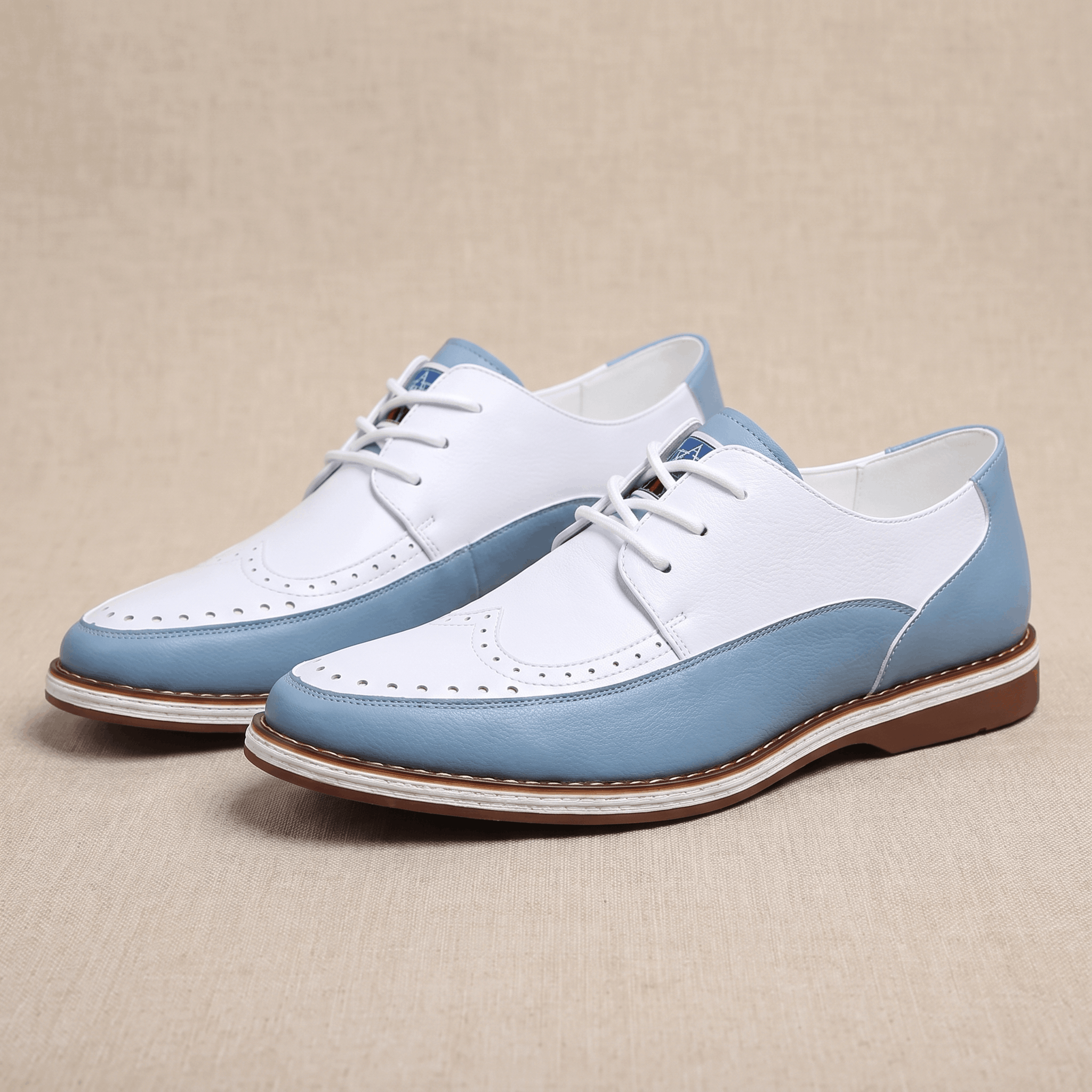 Pair of white and blue two-tone leather Mauro brogues angled together on a beige surface, showing perforated detailing along the toe