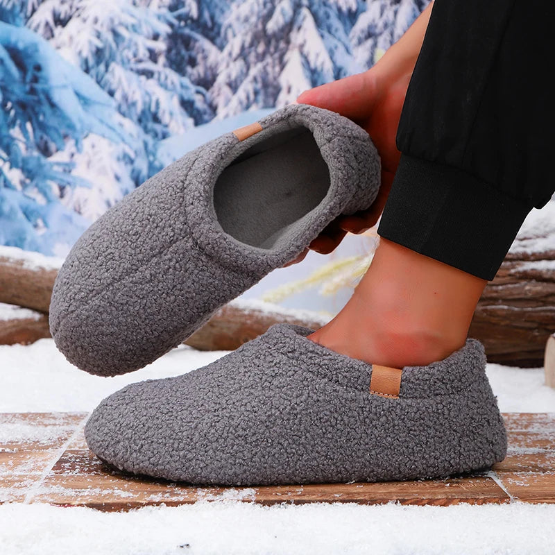 A person putting on a gray teddy fleece slide while standing on a snowy wooden bench outdoors.
