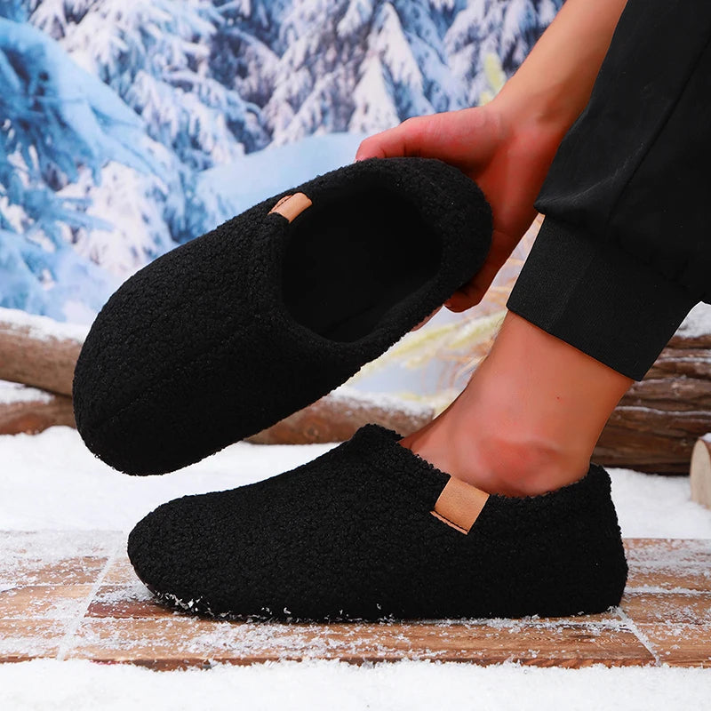 A person putting on a black teddy fleece slide while standing on a snowy wooden bench outdoors.