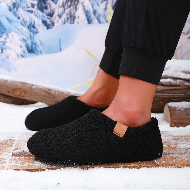 A model's ankles wearing black teddy fleece slides, standing on a snowy wooden bench outdoors.