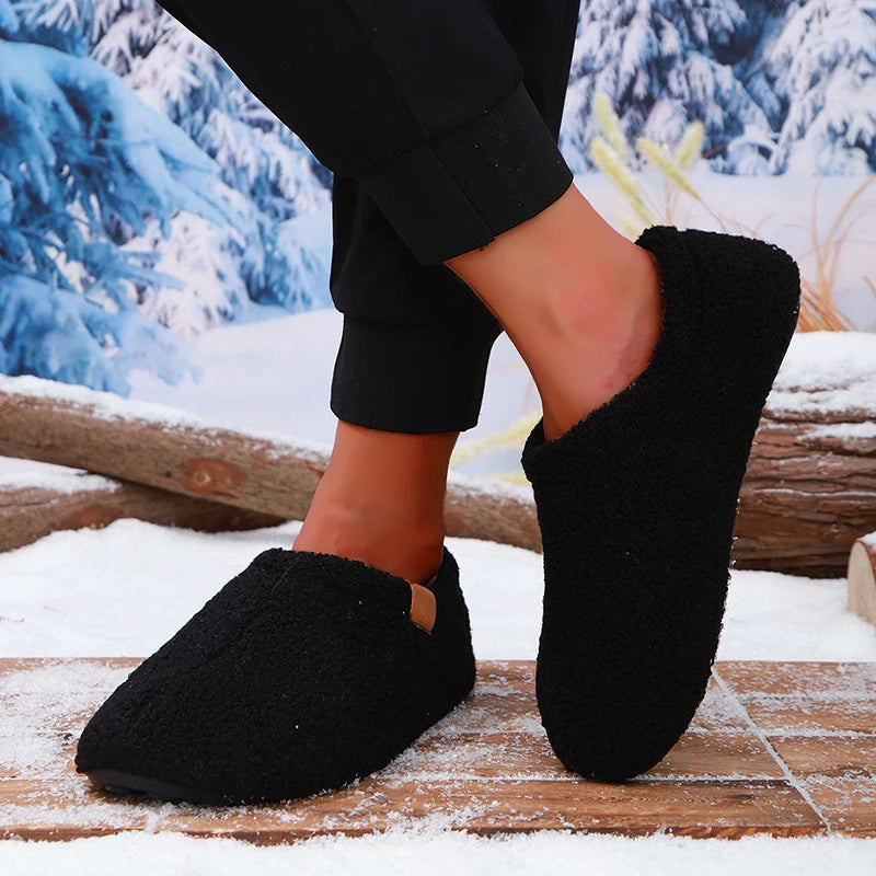 A person mid-step wearing black teddy fleece slides, one foot lifted, on a snowy wooden bench outdoors.