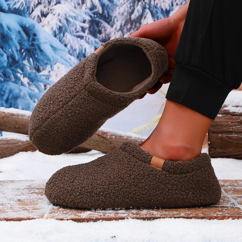 A person putting on a brown teddy fleece slide while standing on a snowy wooden bench outdoors.