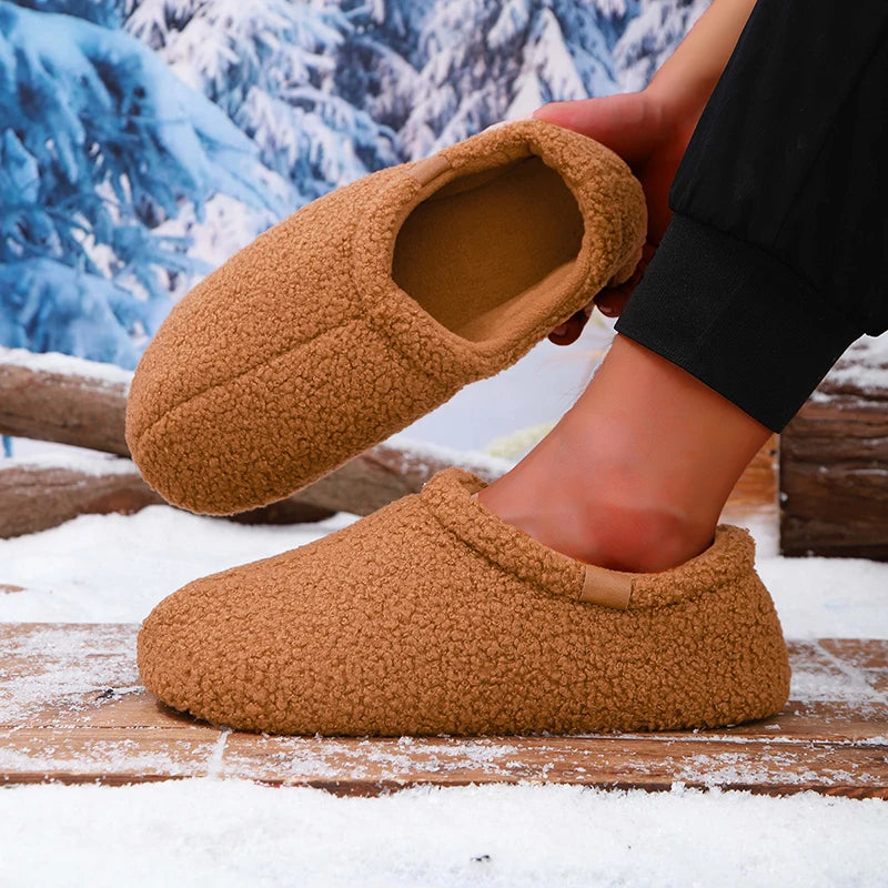 A person putting on a tan teddy fleece slide while standing on a snowy wooden bench outdoors.