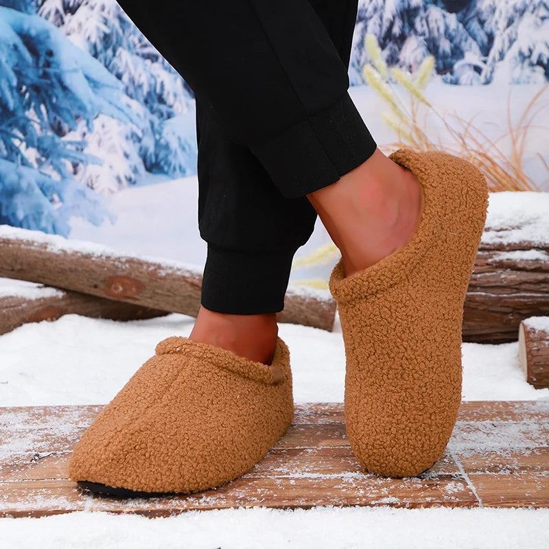 A model's ankles wearing tan teddy fleece slides, standing on a snowy wooden bench outdoors.