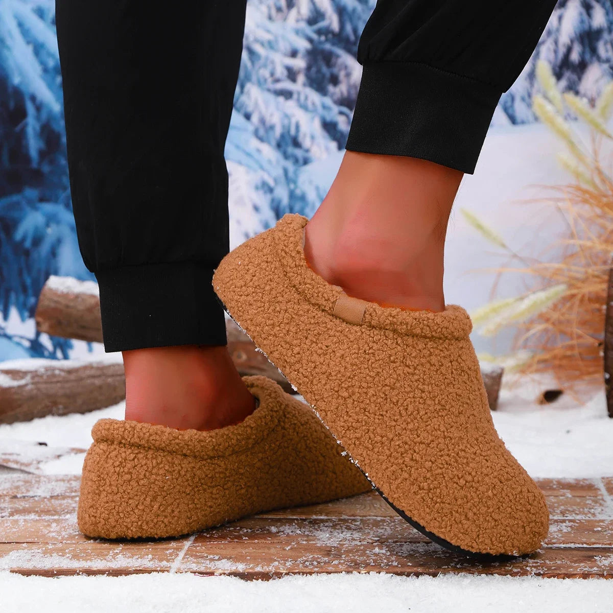 A person mid-step wearing tan teddy fleece slides, one foot lifted, on a snowy wooden bench outdoors.