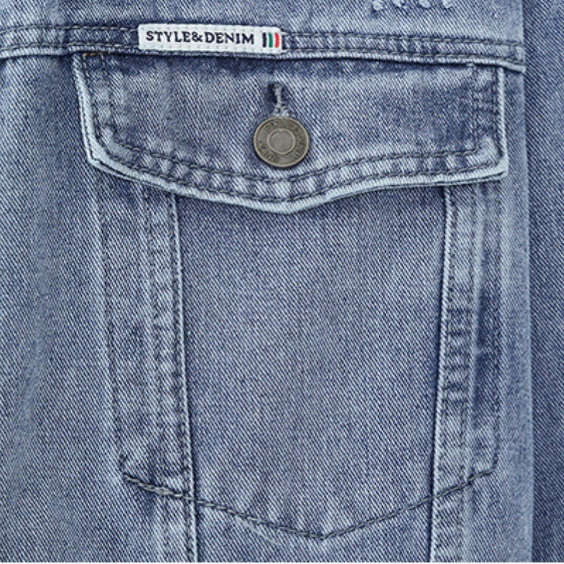 Close-up of the button-flap chest pocket on a men's light wash denim trucker jacket with contrast stitching.
