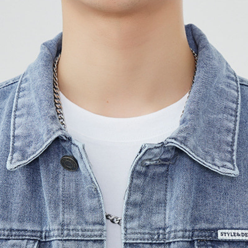 Close-up of the pointed collar and upper front of a men's light wash denim trucker jacket layered over a white T-shirt.