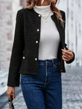 Woman wearing a black textured tweed jacket with gold-tone buttons over a white ribbed sweater and blue jeans while walking outdoors.