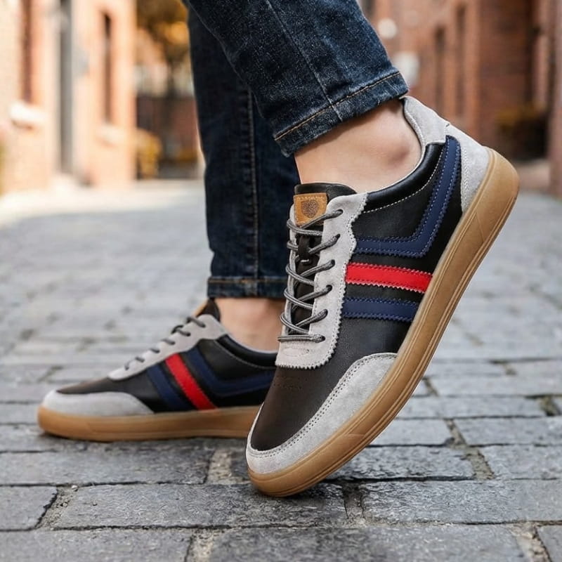 Person wearing black and gray leather retro court sneakers with blue and red stripes and jeans, walking on a cobblestone street