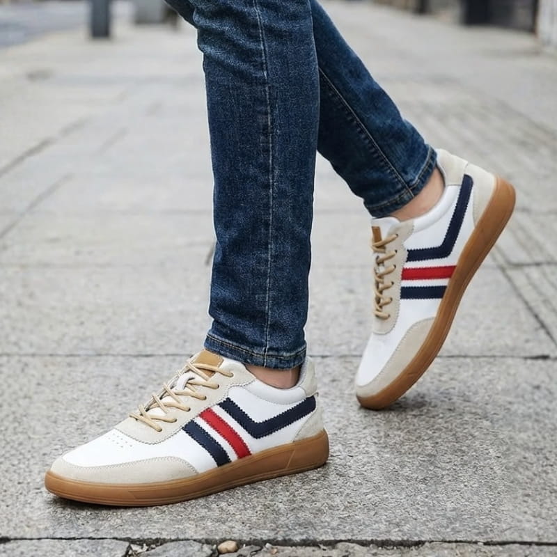Person wearing white leather retro court sneakers with navy and red stripes and jeans, walking on a cobblestone street