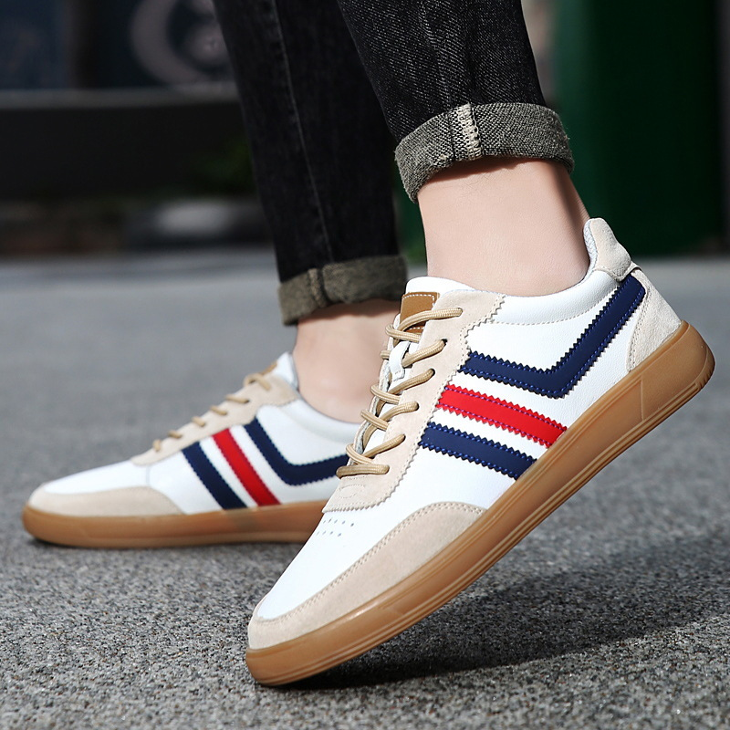 Person wearing white leather retro court sneakers with navy and red stripes and cuffed dark jeans, walking on pavement