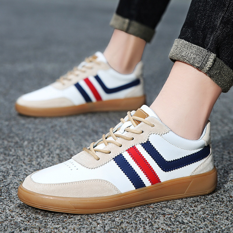 Close-up of a white leather retro court sneaker with navy and red stripes worn with cuffed jeans on a paved surface