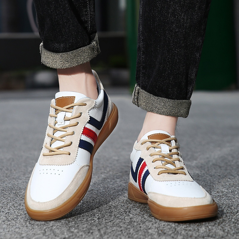 Person wearing white leather retro court sneakers with navy and red stripes, both feet visible walking on pavement