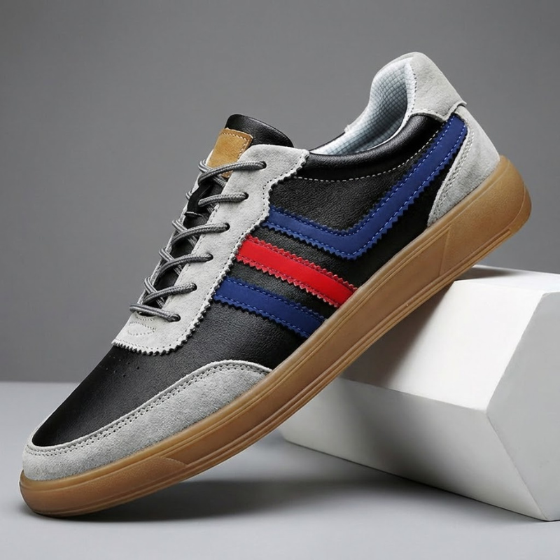Black and gray leather retro court sneaker with blue and red side stripes and gum sole propped diagonally against a white block