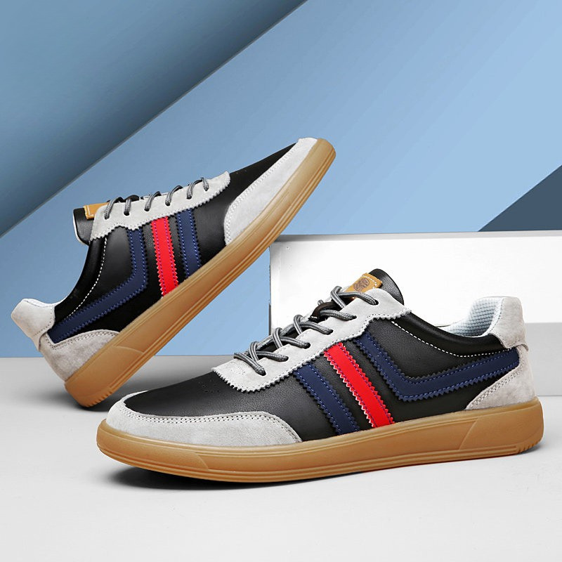 Pair of black and gray leather retro court sneakers with blue and red stripes stacked at an angle on a blue gradient background