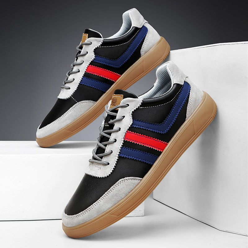 Pair of black and gray leather retro court sneakers with blue and red stripes propped on a white platform against a gray background