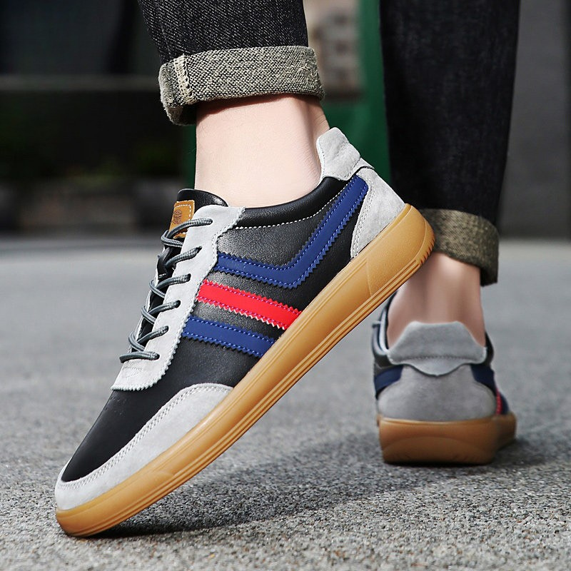 Person wearing black and gray leather retro court sneakers with blue and red stripes and cuffed dark jeans, walking on pavement