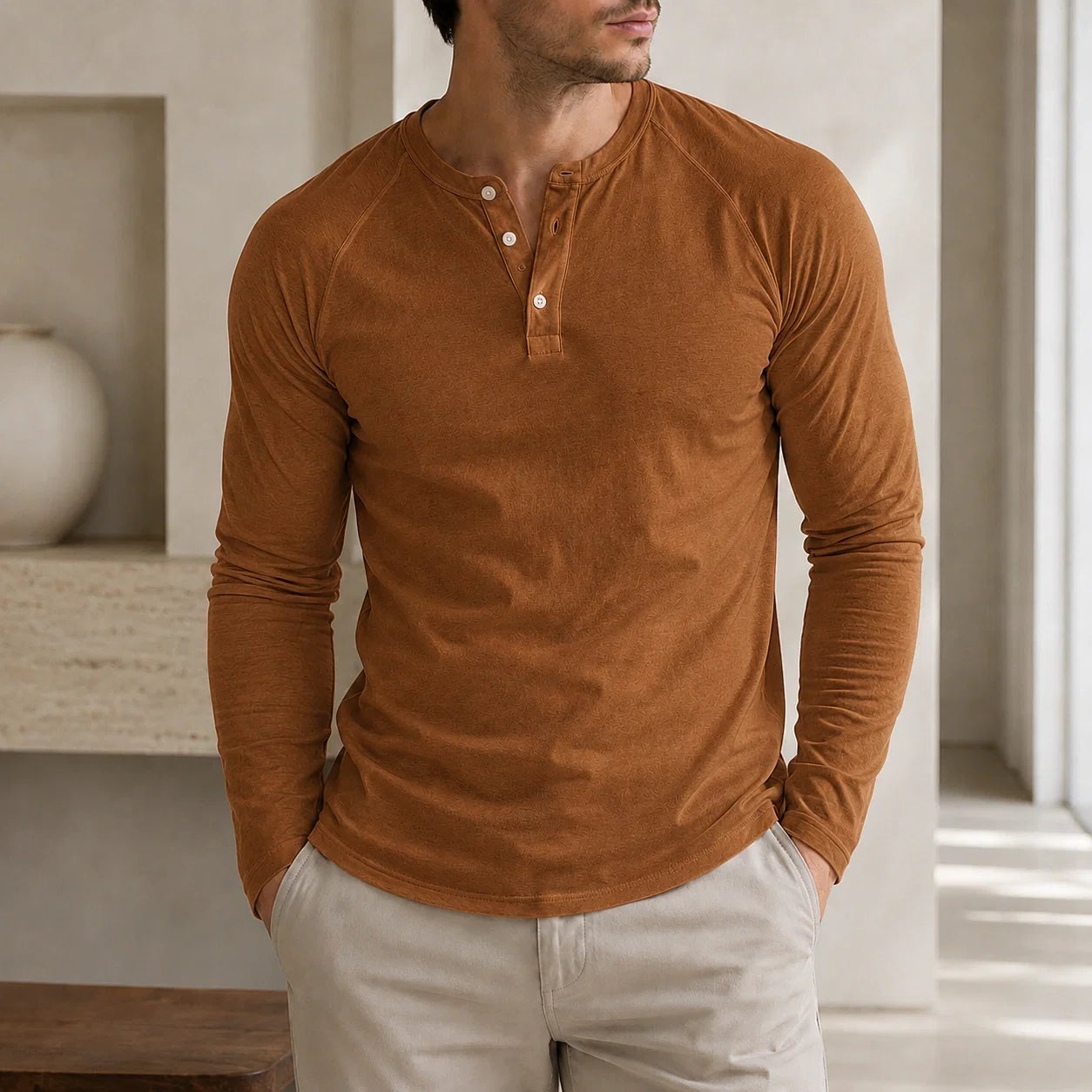 Man wearing a brown long-sleeve Henley sweater featuring a three-button placket, ribbed cuffs, and a fitted silhouette.