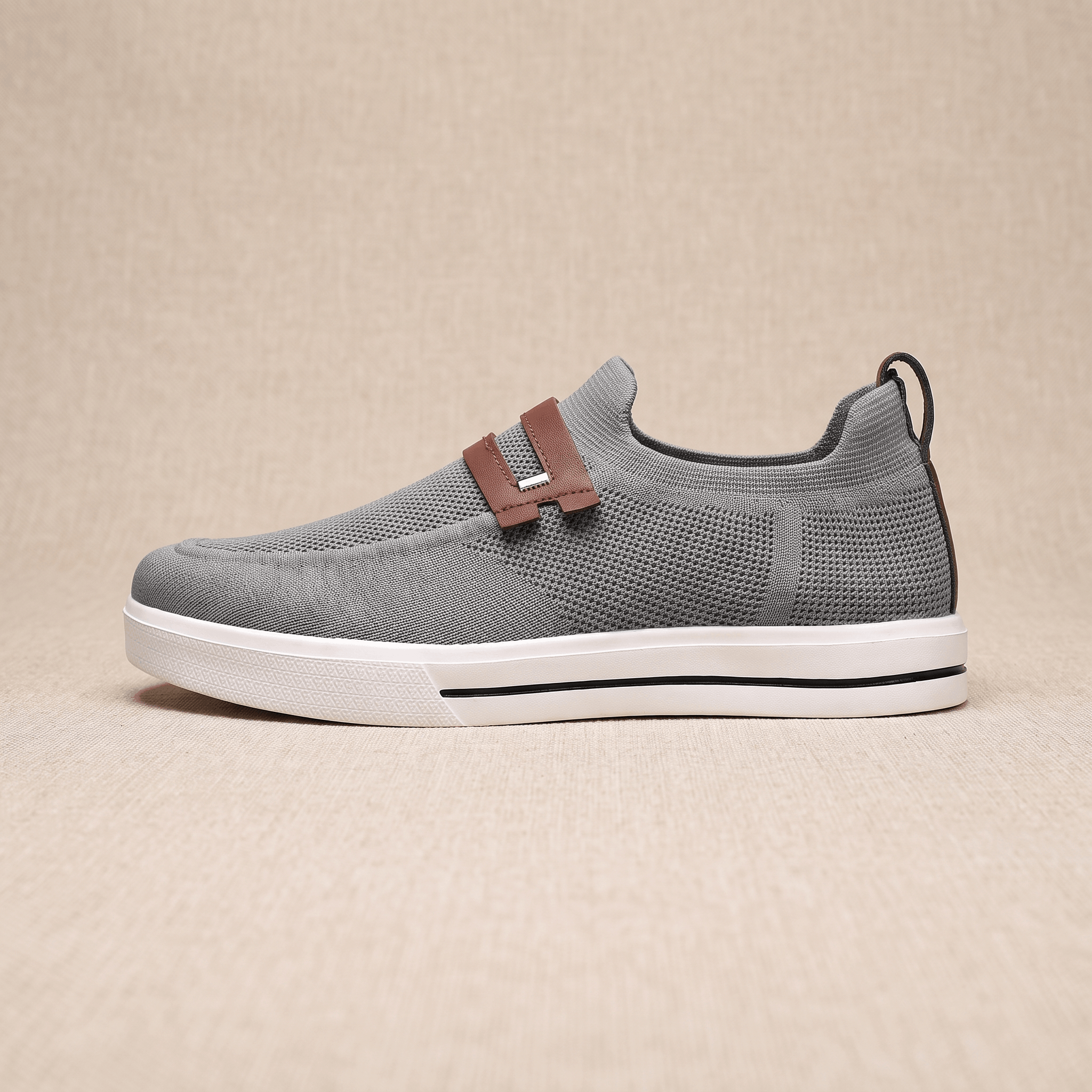 Side profile of a single gray mesh Orion sneaker with brown leather strap, resting on a beige surface