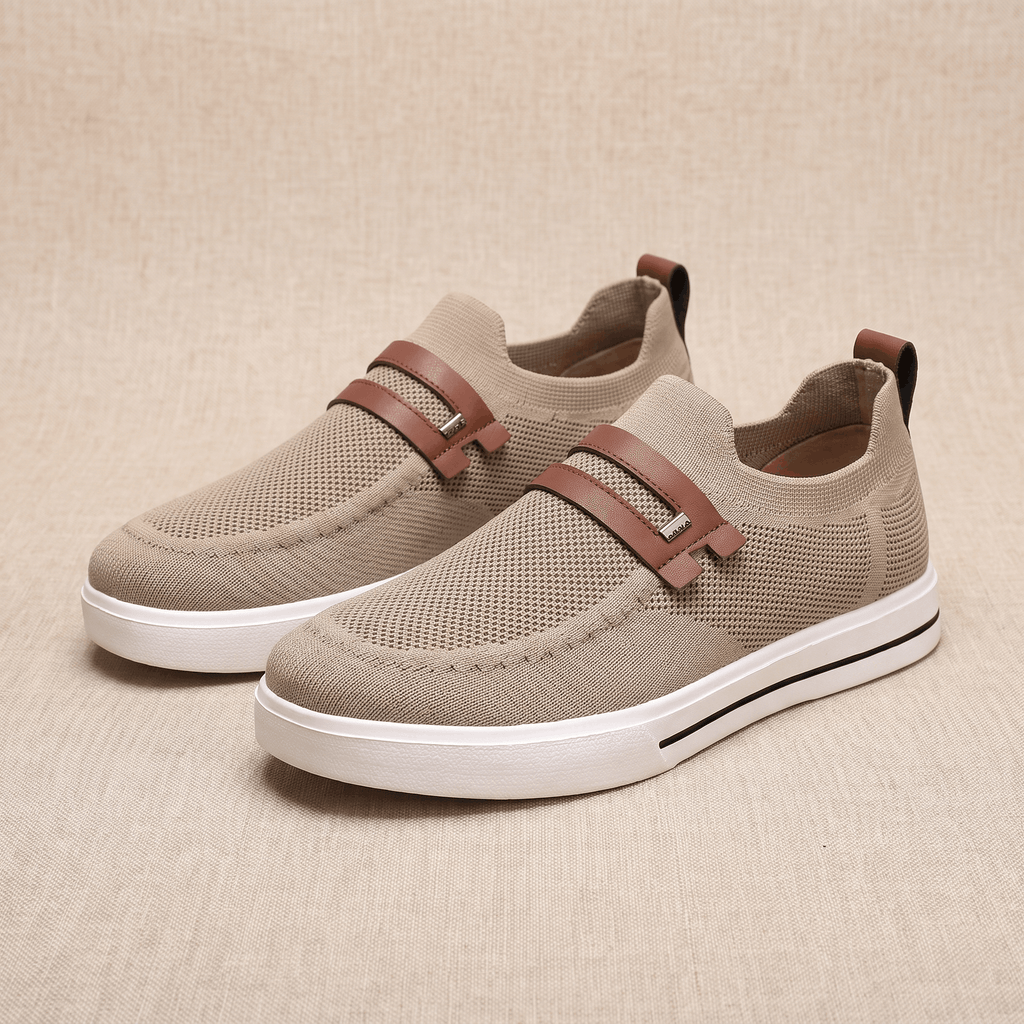 Pair of khaki mesh Orion slip-on sneakers with brown leather straps, resting on a beige fabric backdrop