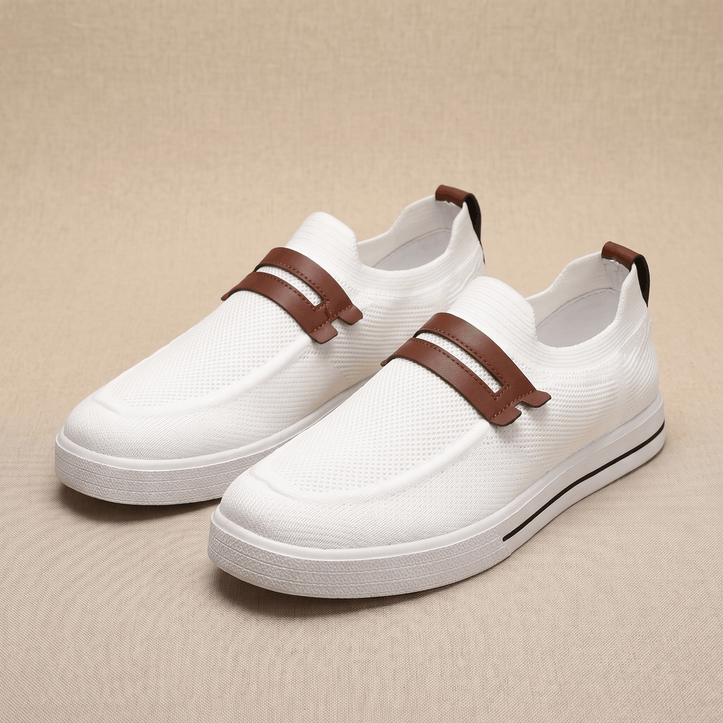 Pair of white mesh Orion slip-on sneakers with brown leather straps, resting on a beige fabric backdrop