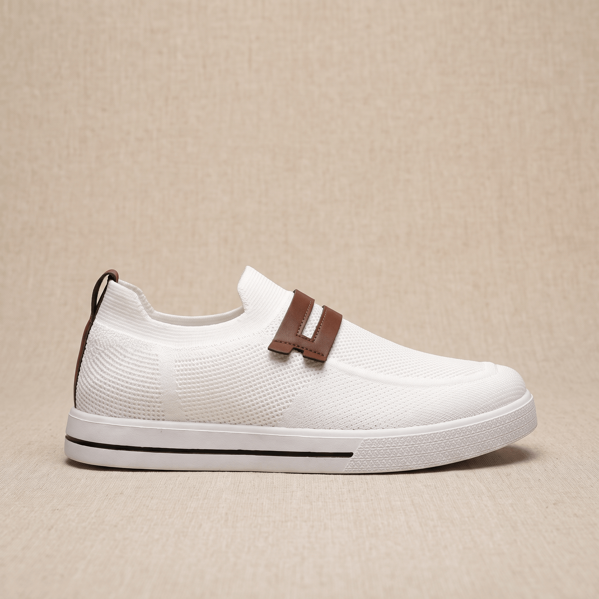 Side profile of a single white mesh Orion sneaker with brown leather strap and pull tab, resting on a beige surface