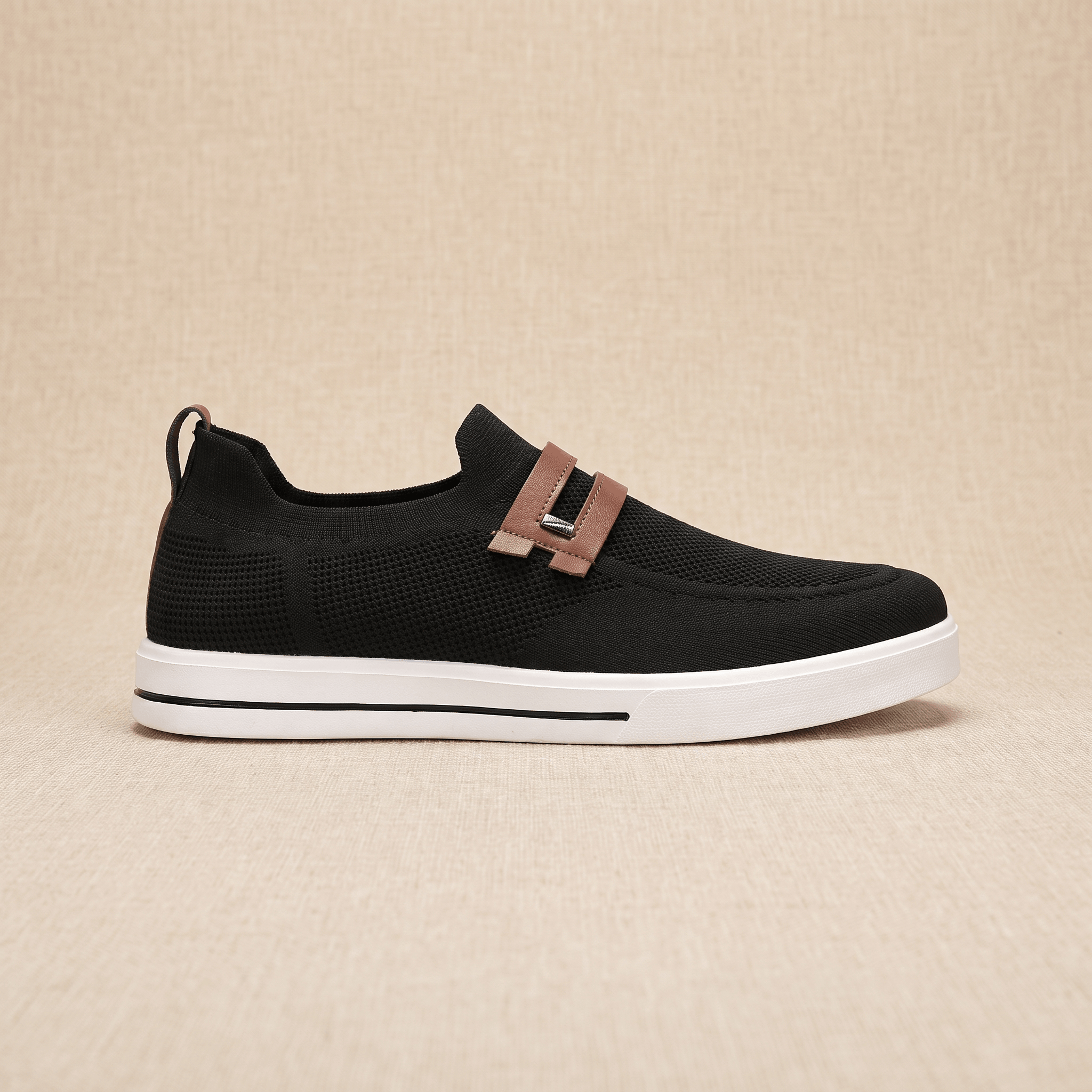 Side profile of a single black mesh Orion sneaker with brown leather strap, resting on a beige surface