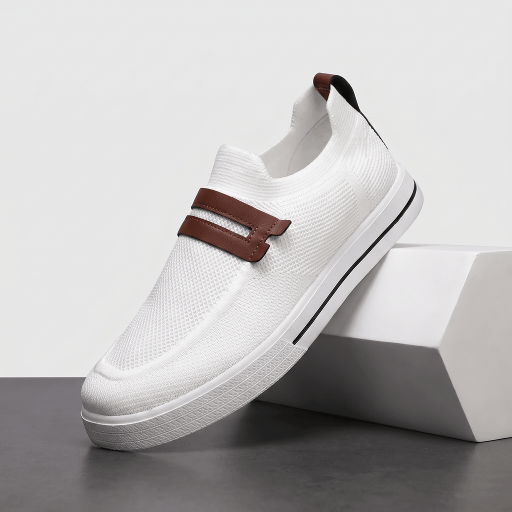 Single white mesh Orion slip-on sneaker with brown leather strap accent, angled on a white block against a studio backdrop
