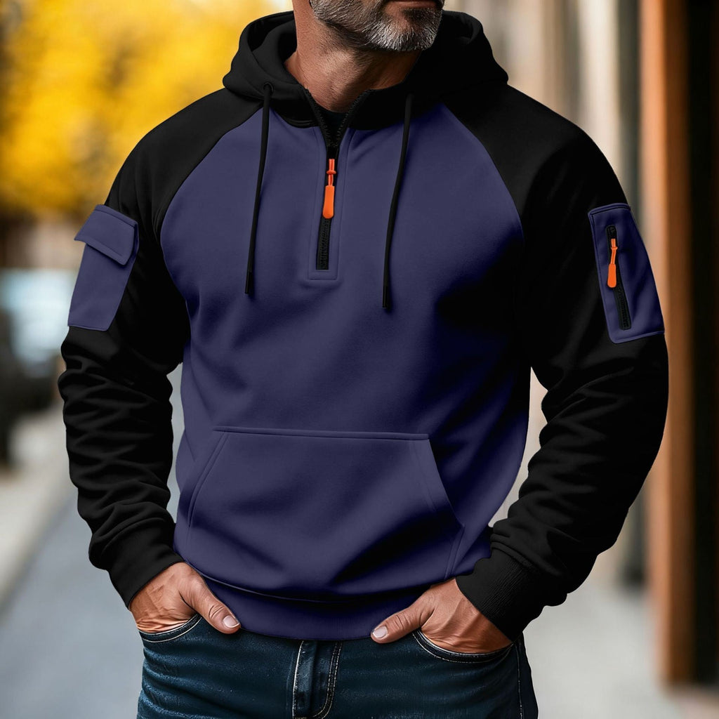 Man wearing a navy and black color-block tactical hoodie with a half-zip neckline, adjustable hood, utility sleeve pocket, and front kangaroo pocket.