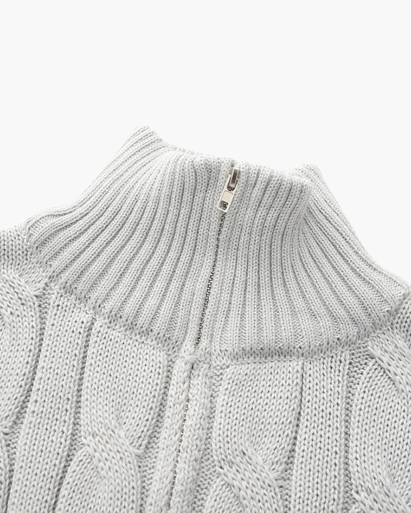 Close-up of a light gray cable knit quarter-zip sweater showcasing the ribbed stand collar and textured knit pattern.