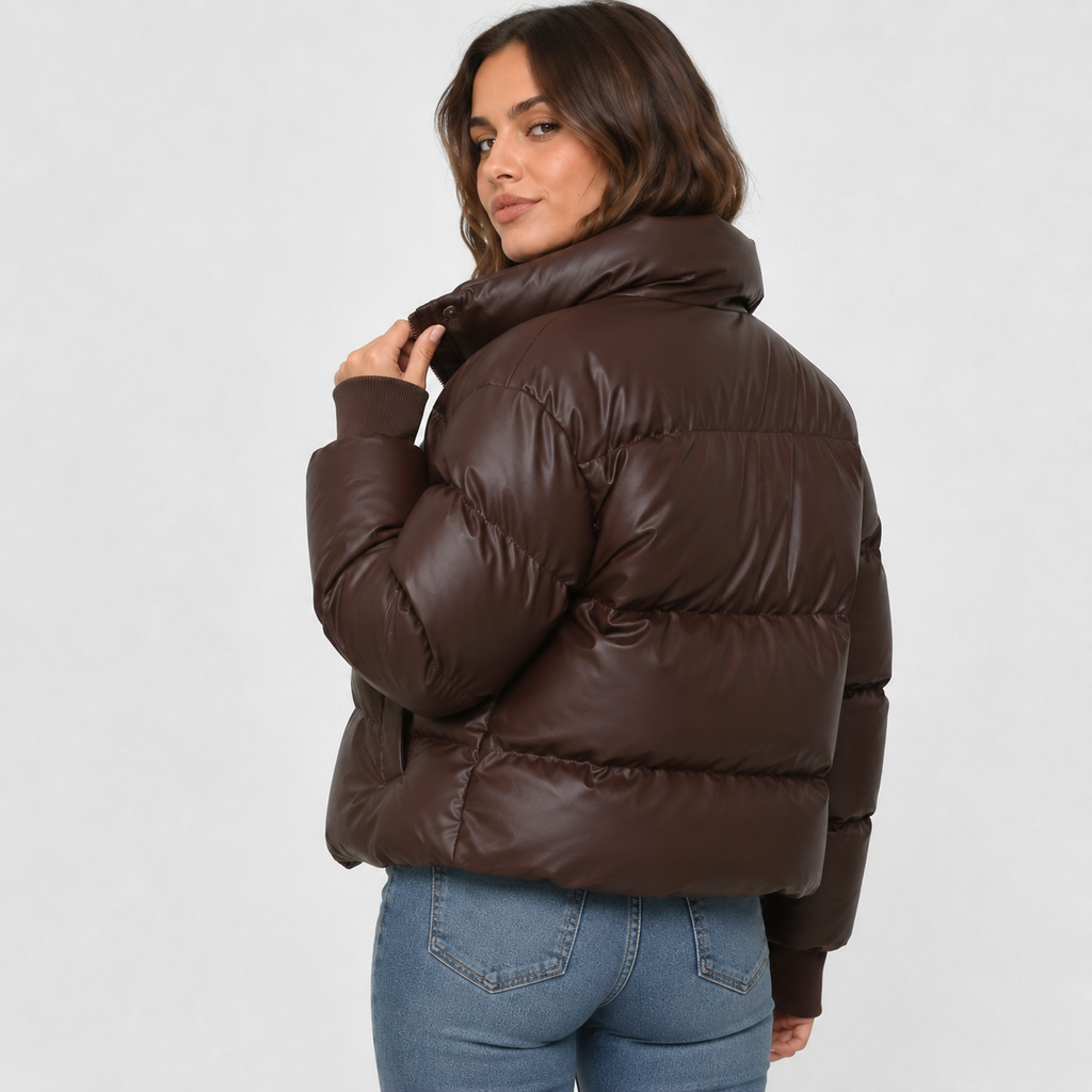 Dark brown cropped puffer jacket with a stand collar, quilted padding, and snap-over zip front worn with blue jeans.