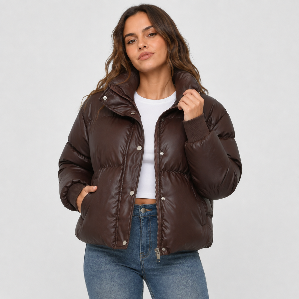 Dark brown cropped puffer jacket with a stand collar, snap-over zip front, and ribbed cuffs worn over a white top.