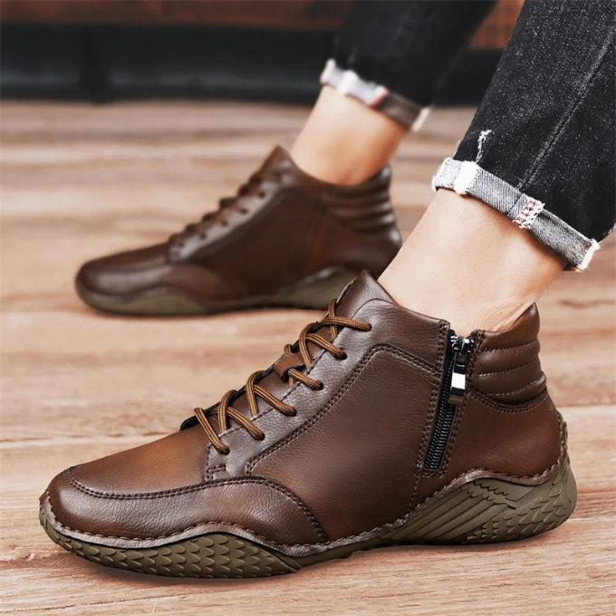 A model's ankles in cuffed jeans wearing brown leather zip-up ankle boots, standing on a wooden floor.