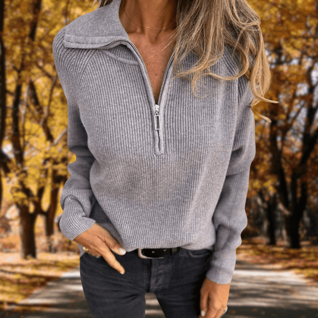 Woman wearing a light gray ribbed quarter-zip knit sweater with a high collar, long sleeves, and a relaxed fit in an outdoor setting.