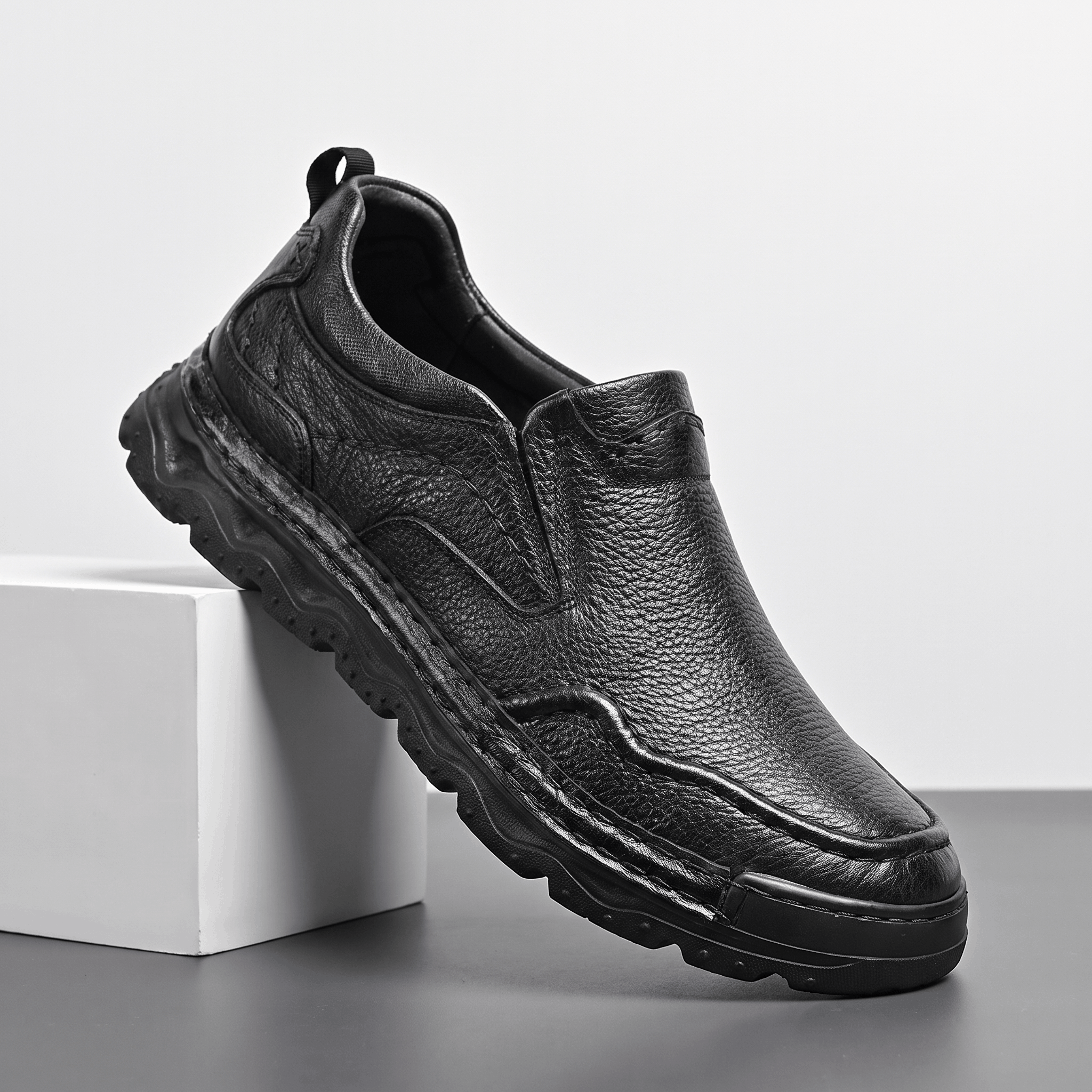 Side view of a single black leather Piolo loafer propped against a white block, showing chunky sole and pull tab