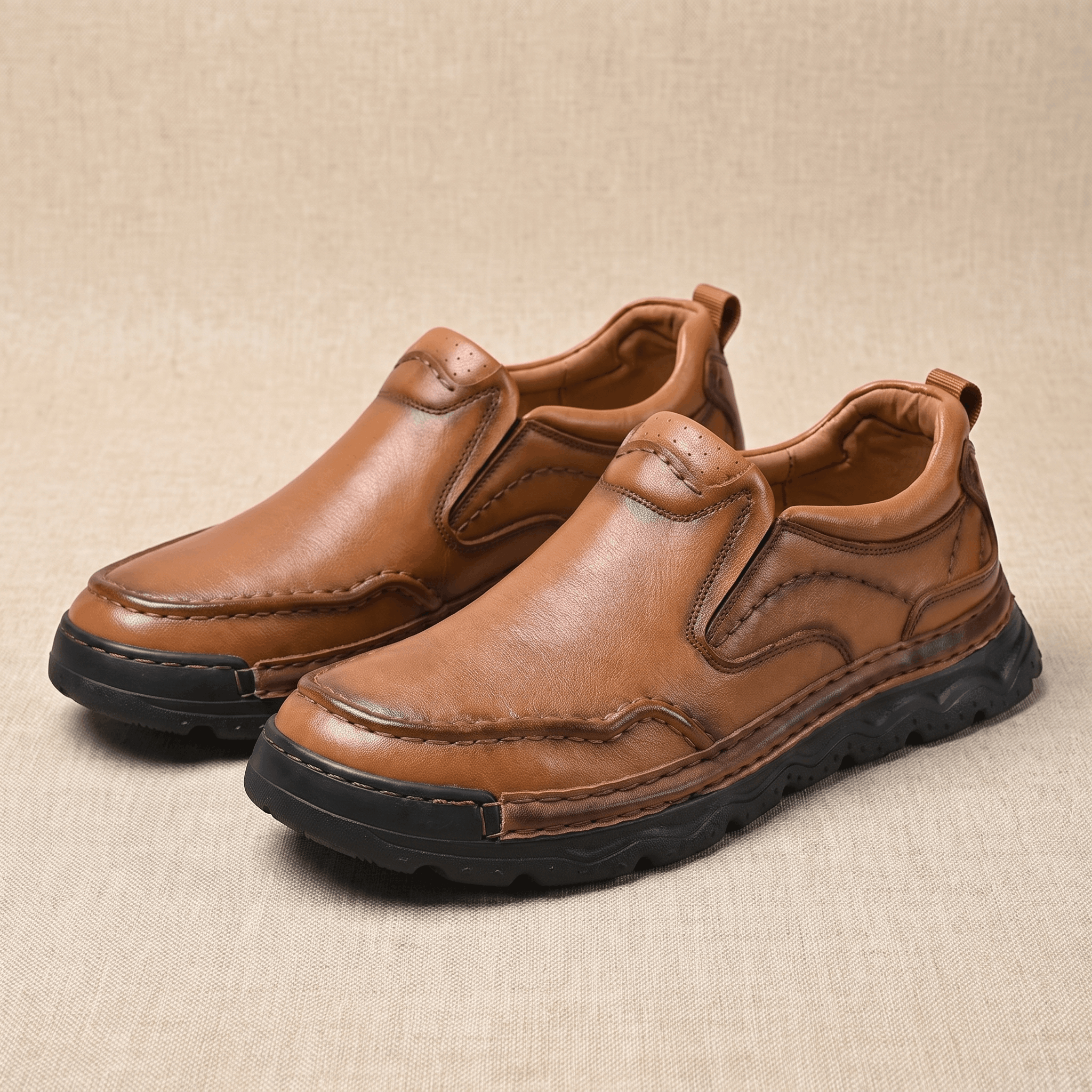 Pair of brown leather Piolo slip-on loafers with contour stitching, resting on a beige fabric backdrop