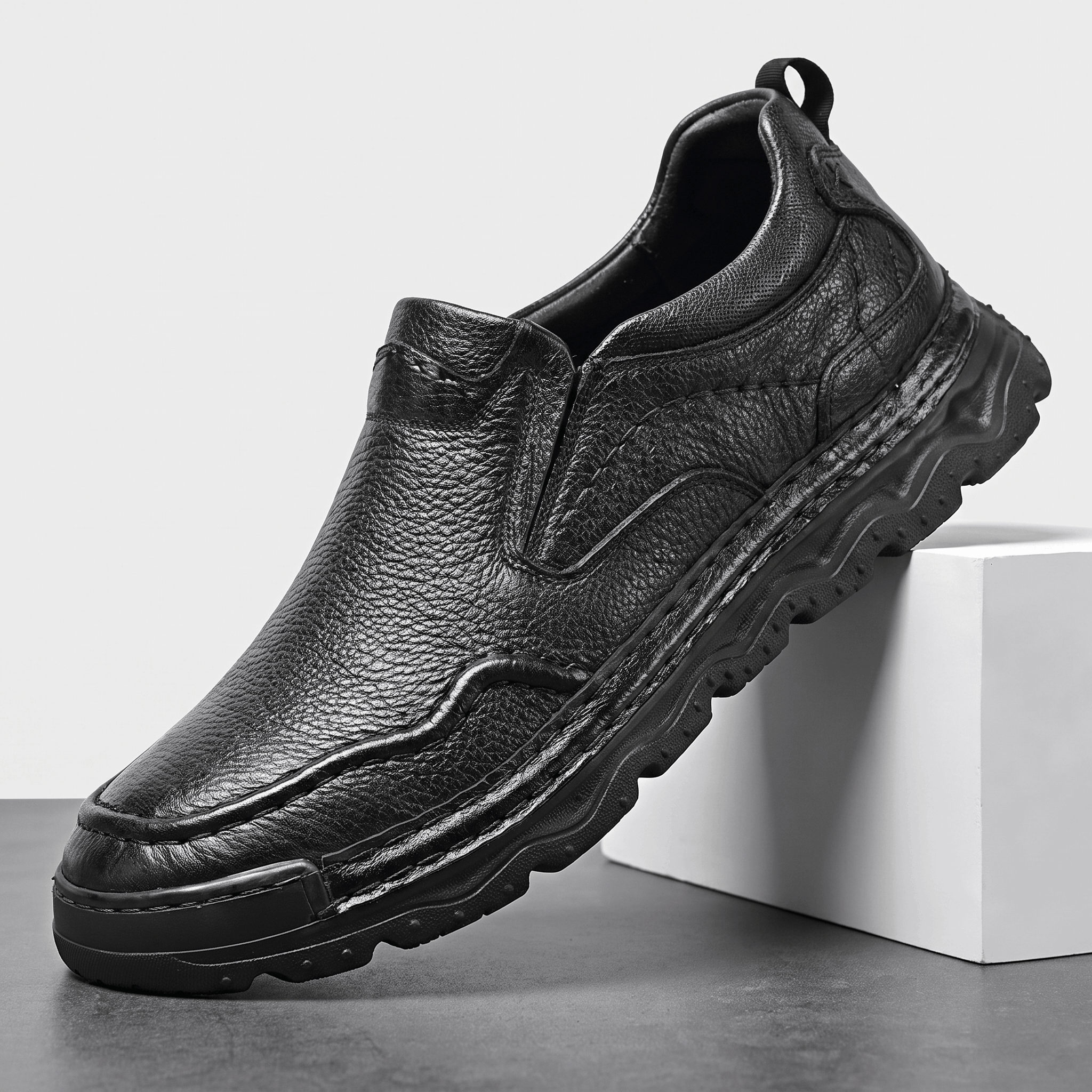 Single black leather Piolo slip-on loafer with pull tab and chunky sole, angled on a white block against a studio backdrop