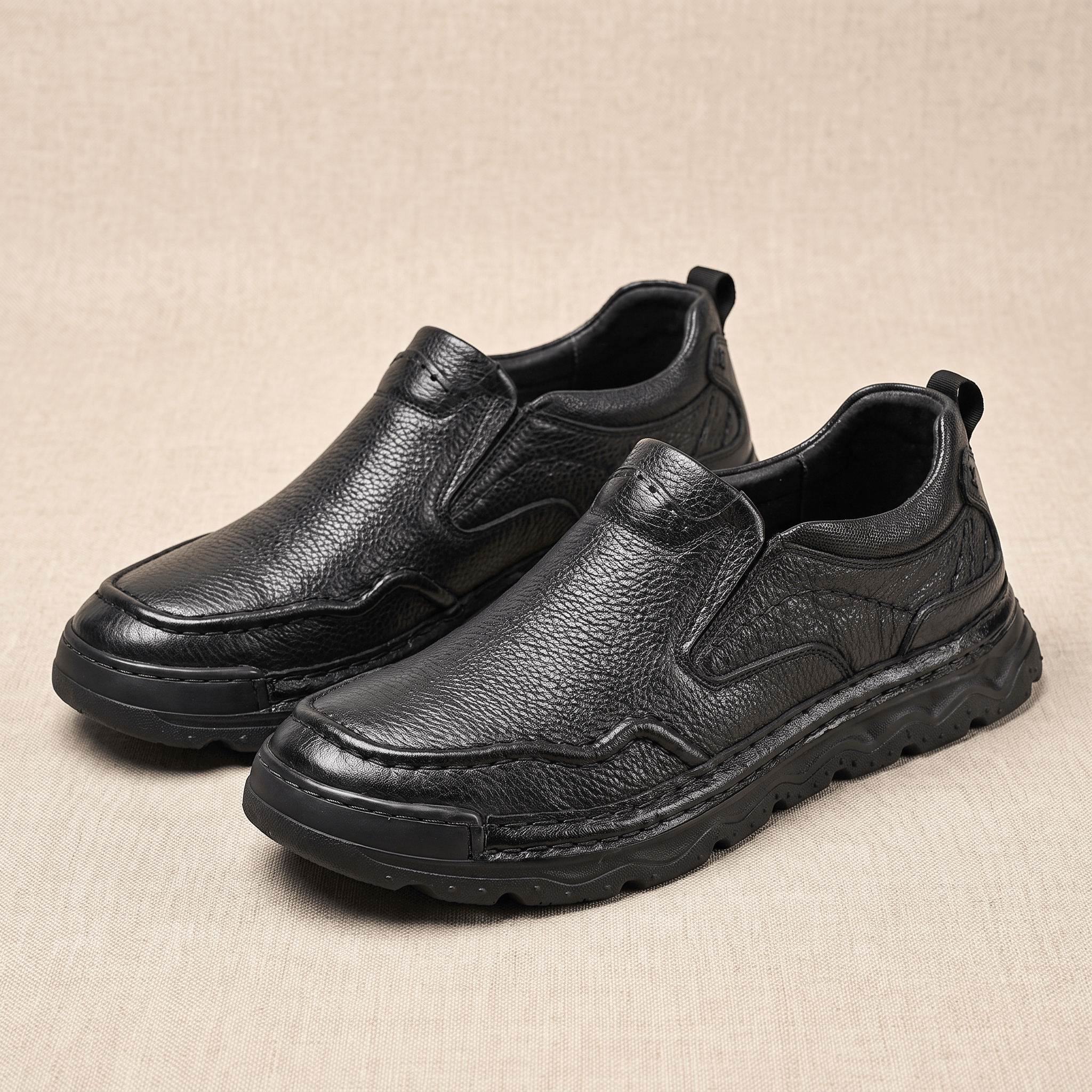 Pair of black leather Piolo slip-on loafers, resting on a beige fabric backdrop