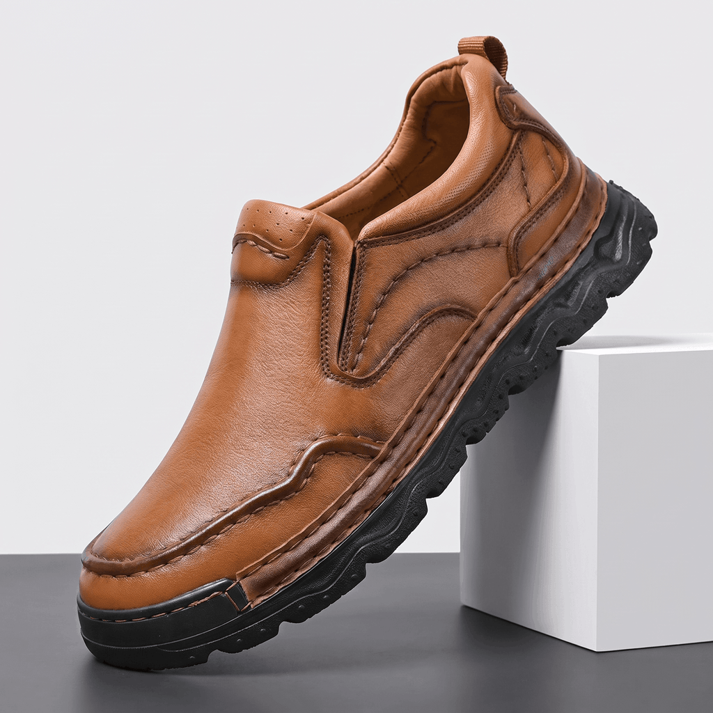Single brown leather Piolo slip-on loafer with contour stitching and chunky black rubber sole, angled on a white block against a studio backdrop