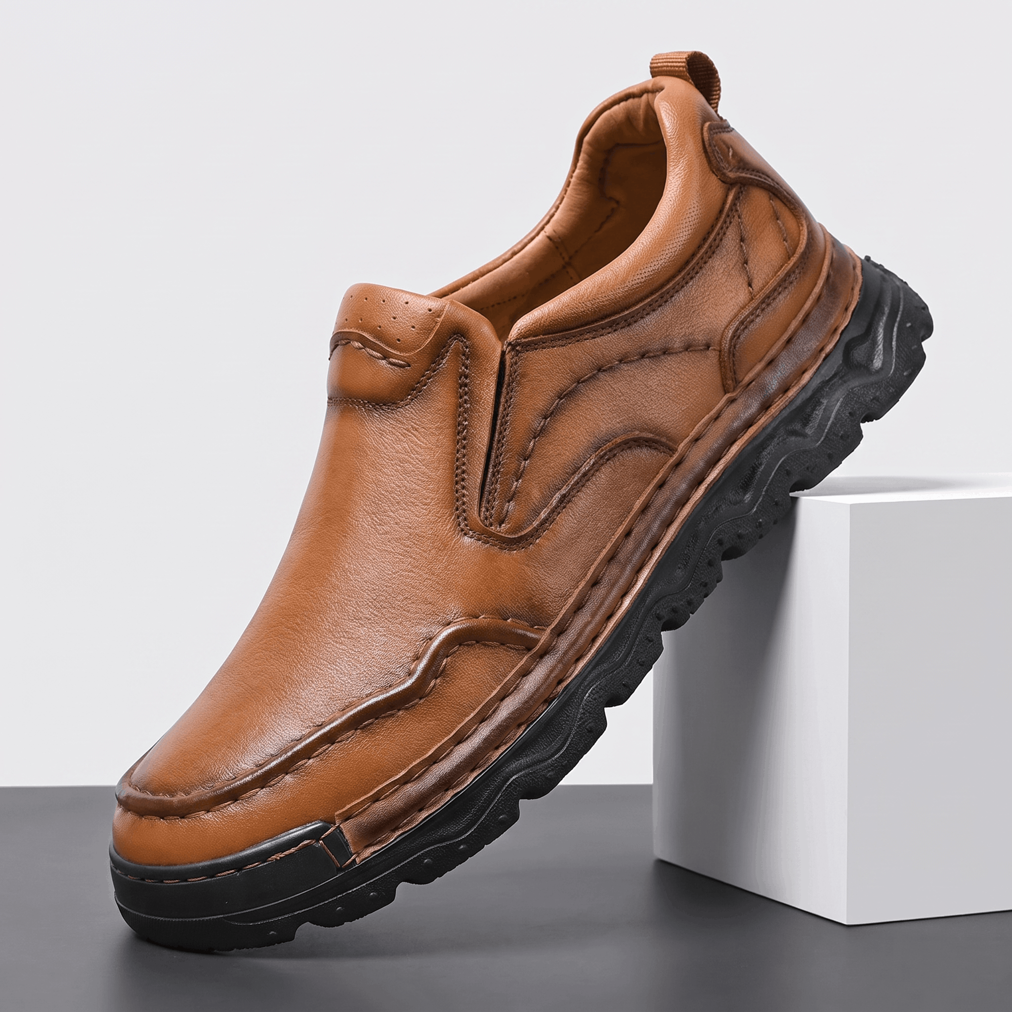 Single brown leather Piolo slip-on loafer with contour stitching and chunky black rubber sole, angled on a white block against a studio backdrop