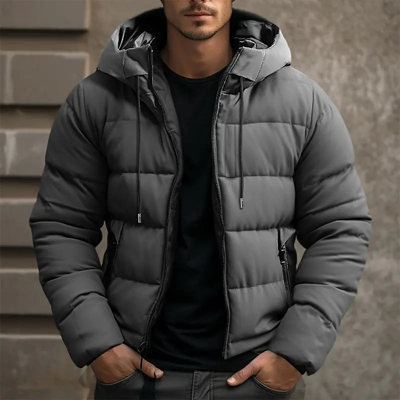 Charcoal gray quilted puffer jacket with a drawstring hood, full-zip front, and tailored fit worn over a black shirt.