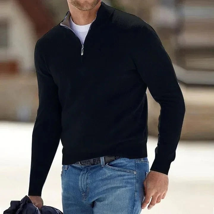 Black half-zip knit sweater with a stand collar and long sleeves, worn with blue jeans in an outdoor setting.
