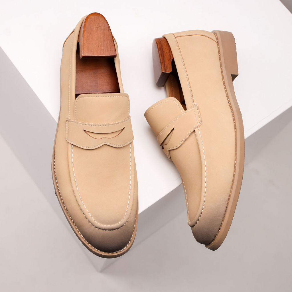 Pair of beige leather penny loafers with wooden shoe trees, propped on angled white geometric blocks.