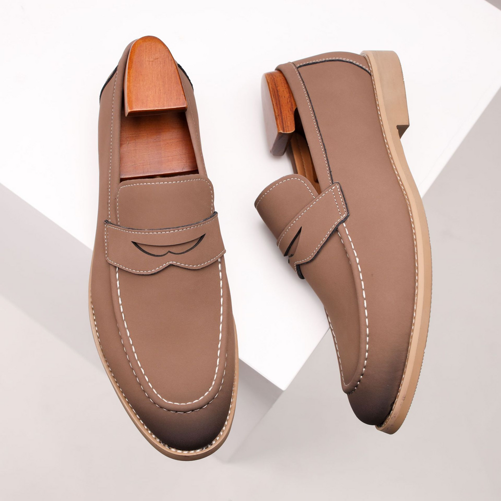 Pair of taupe leather penny loafers with wooden shoe trees, propped on angled white geometric blocks.