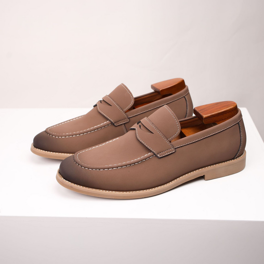 Pair of taupe leather penny loafers with wooden shoe trees, standing on a white surface.