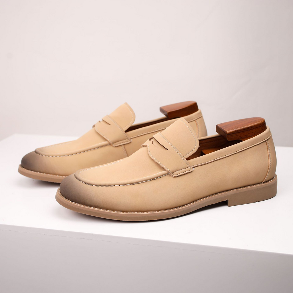 Pair of tan leather penny loafers with burnished toes, standing on a white surface.