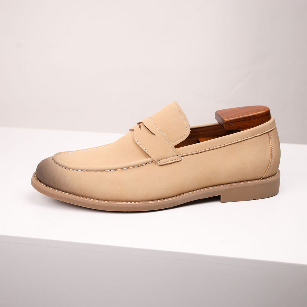 A single tan leather penny loafer with a burnished toe, shown in side profile on a white pedestal.