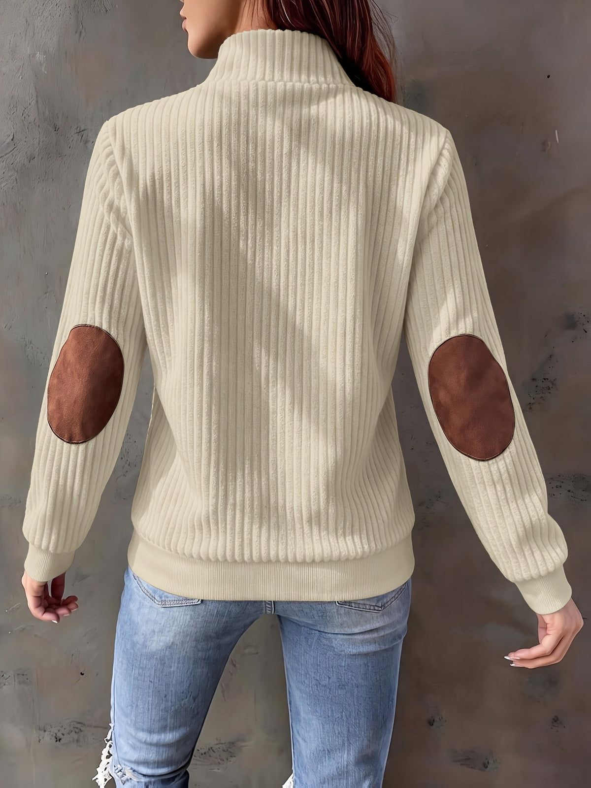 Cream ribbed knit quarter-zip sweater featuring brown suede-look elbow patches and a stand collar, worn with blue jeans.