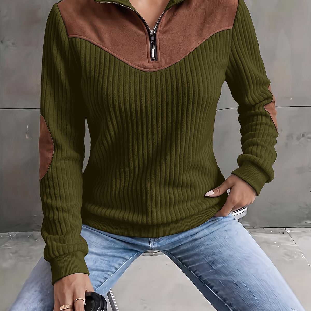 Olive green ribbed knit quarter-zip sweater with brown suede-look yoke and elbow patches, styled with light wash jeans.