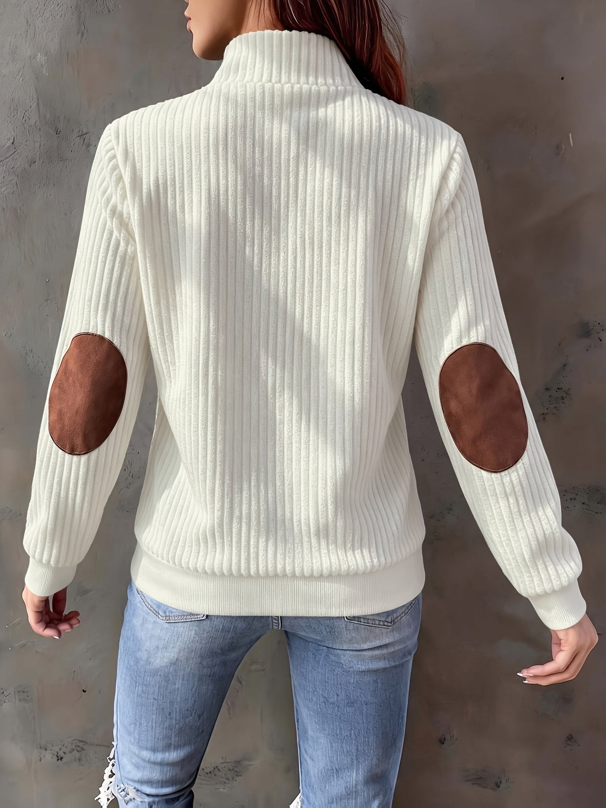 Cream ribbed knit quarter-zip sweater featuring brown suede-look elbow patches and a stand collar, worn with blue jeans.